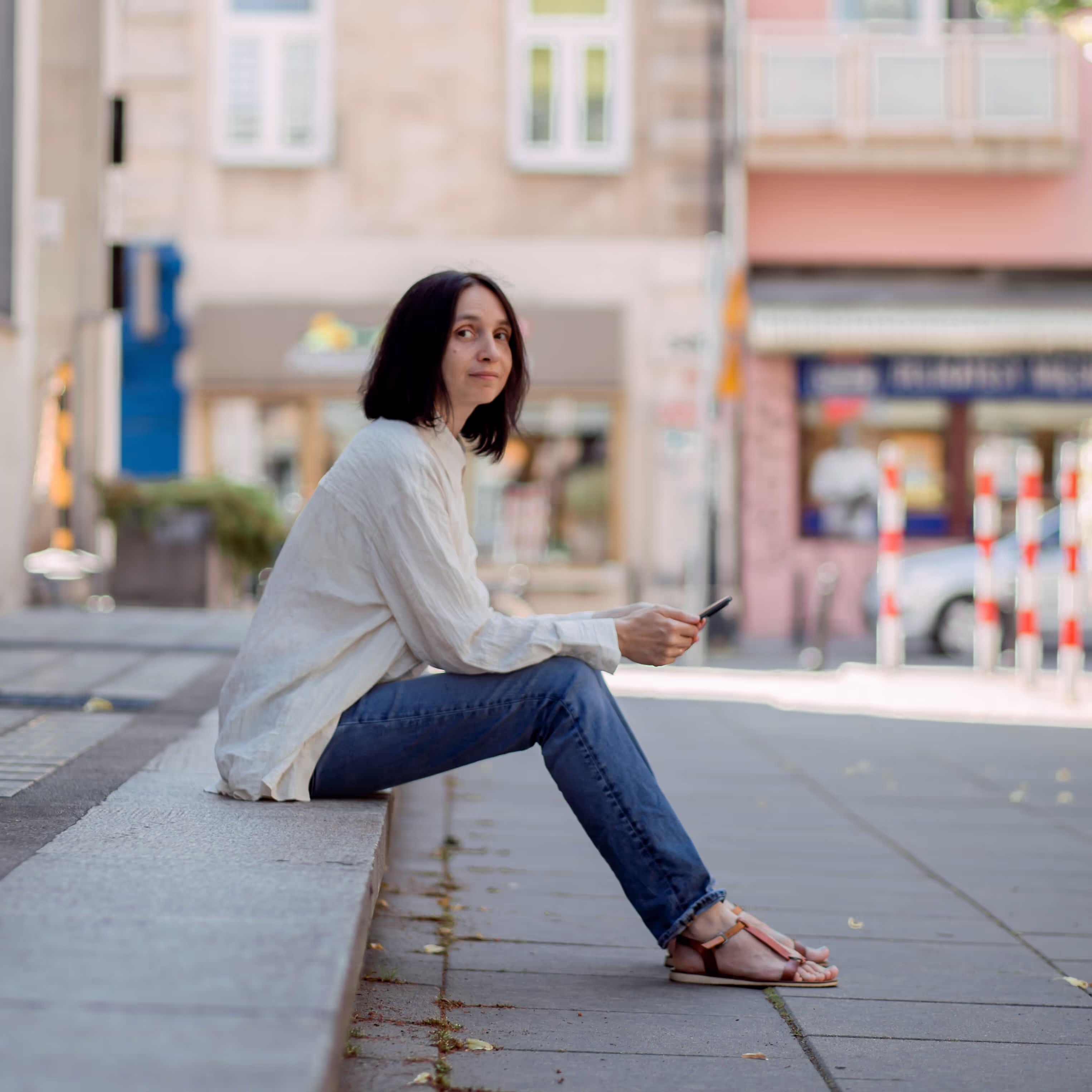 a photo of me, a woman in a white shirt and trousers, with a shoulder long dark straight hair, with a slight smile, sitting with a mobile in her hand.